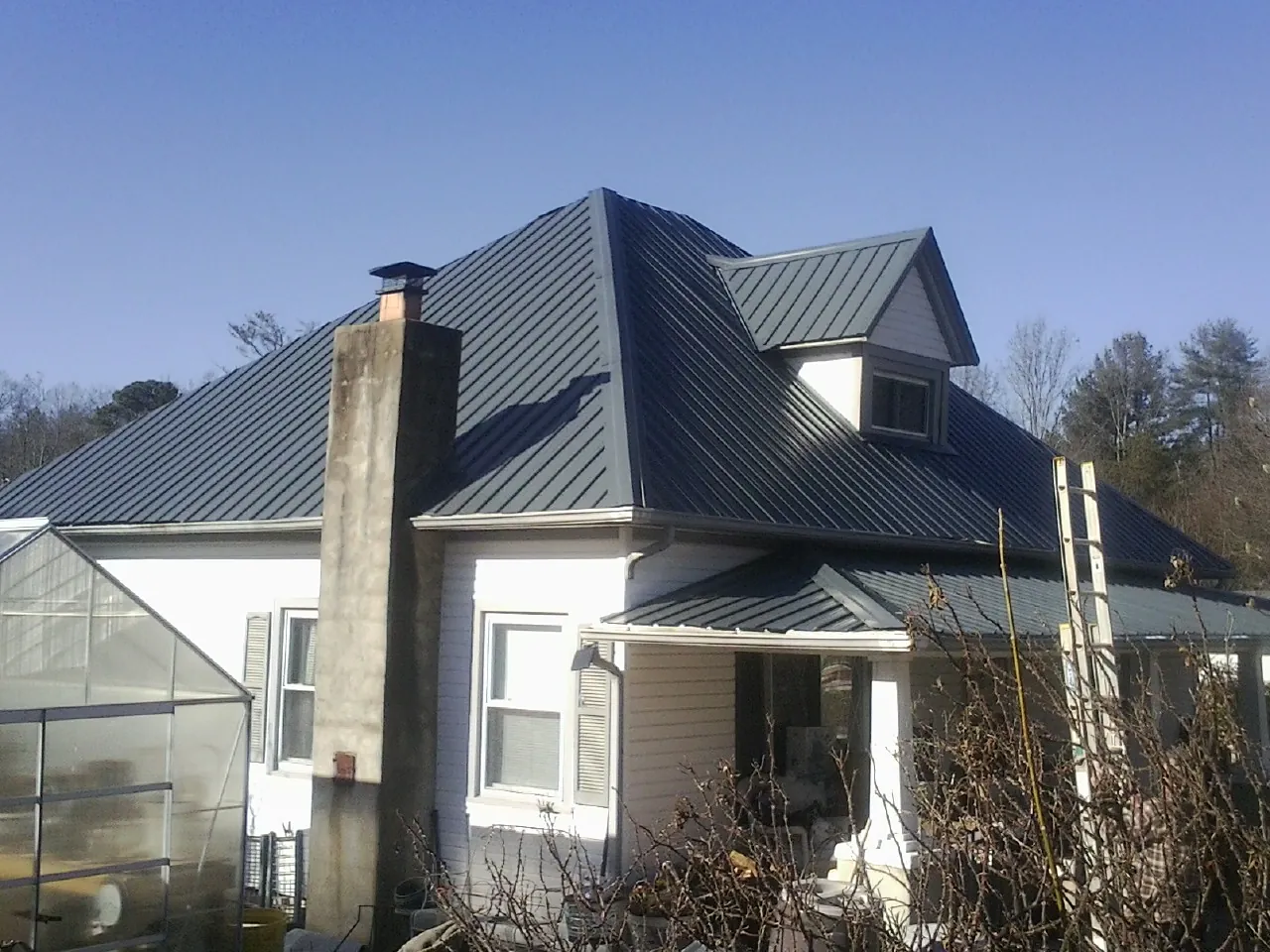 Dark blue standing seam metal roof on a white farmhouse with dormer — Slate & Tile Roof Repair by Roofing Brothers in Fillmore